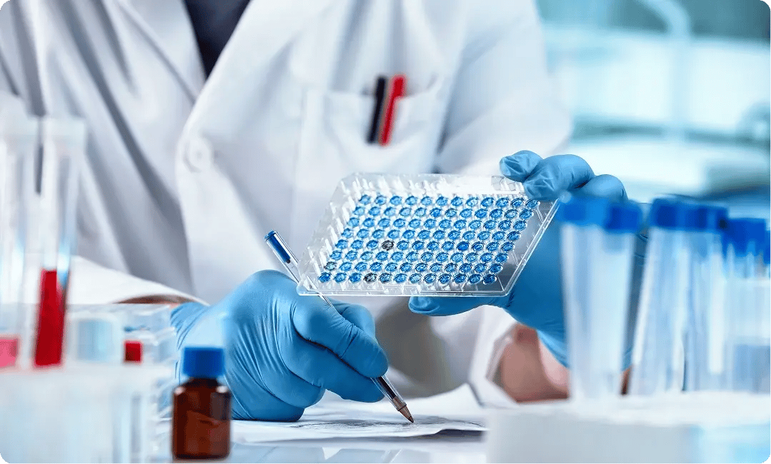 Laboratory researcher examining a microplate during biotech testing.