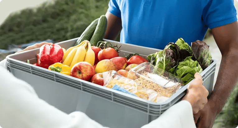 Grocery delivery courier handing a box of fresh produce to a customer