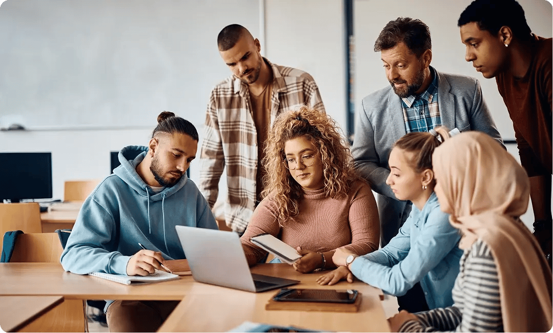 Students and an instructor collaborating around a laptop in a classroom